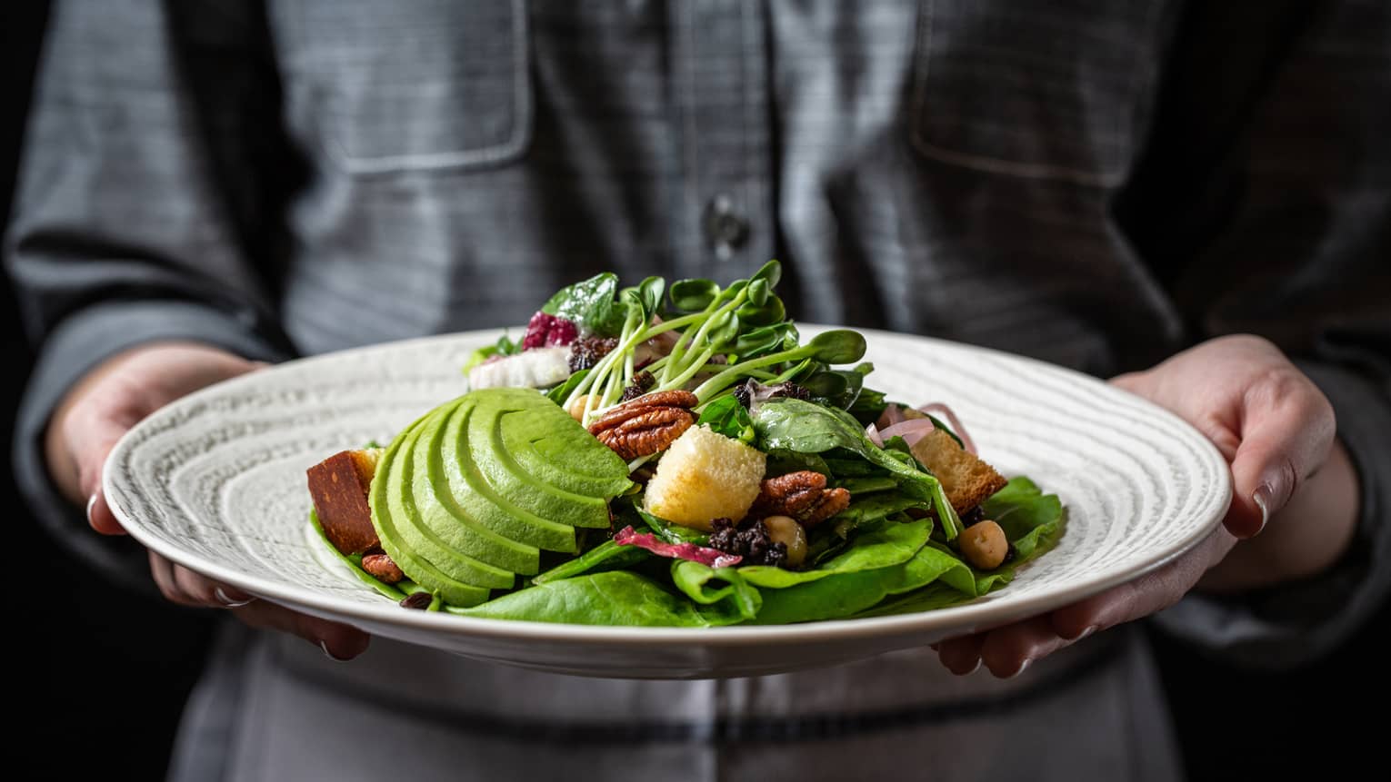 Hotel staff holds plate with large Austin Hippie Salad with avocado slices, fresh greens, walnuts