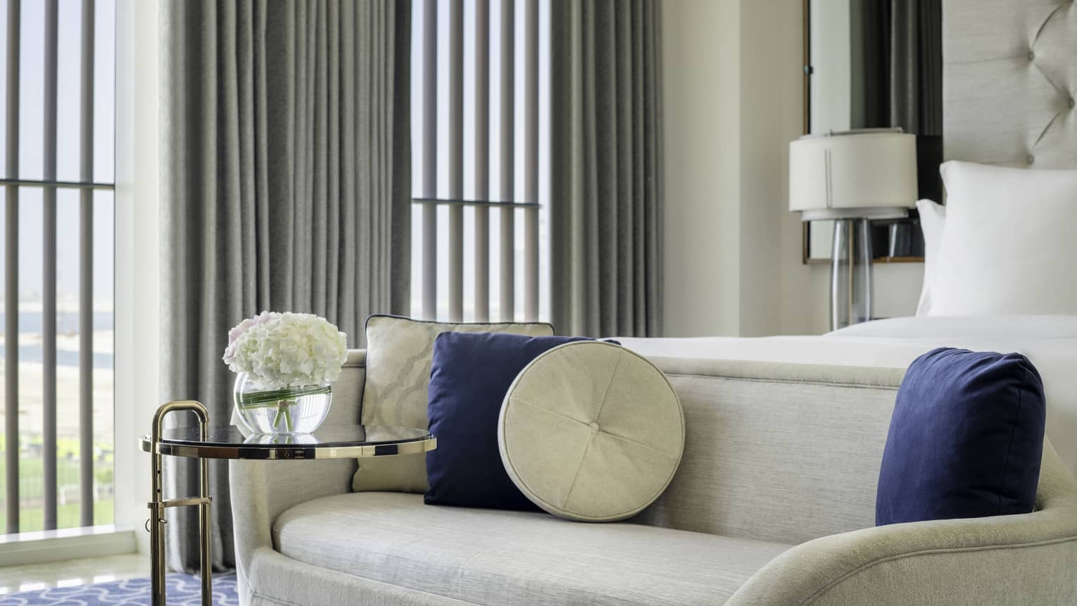 Hotel room with a chaise longue at the foot of a king bed, with small glass table