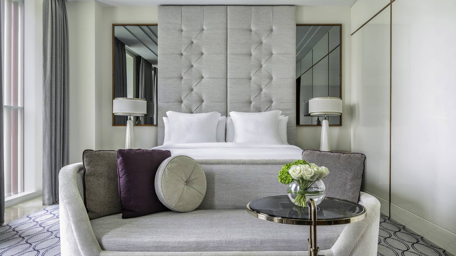 Hotel room with king bed, ceiling-height headboard, chaise longue and small table with flowers