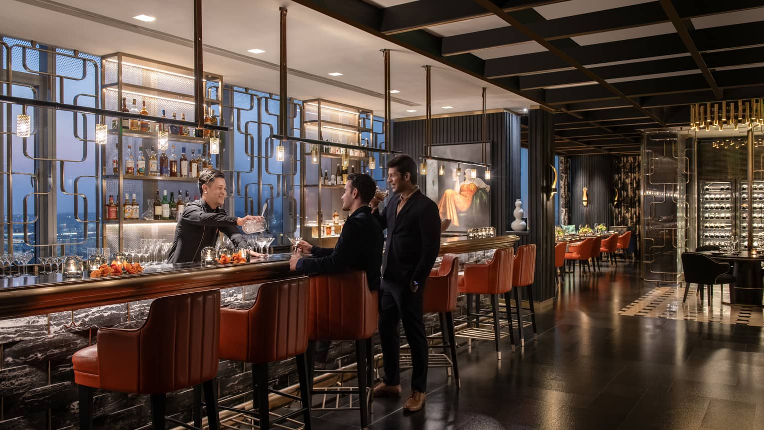 Two people stand at bar as smiling bartender hands them a drink