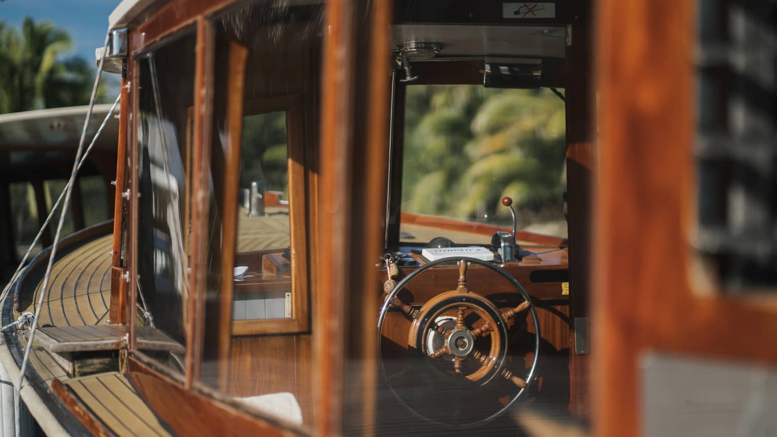 View from outside into a boat's cockpit cabin, both the boat's frame and the wheel partly made of rustic deep-brown wood.