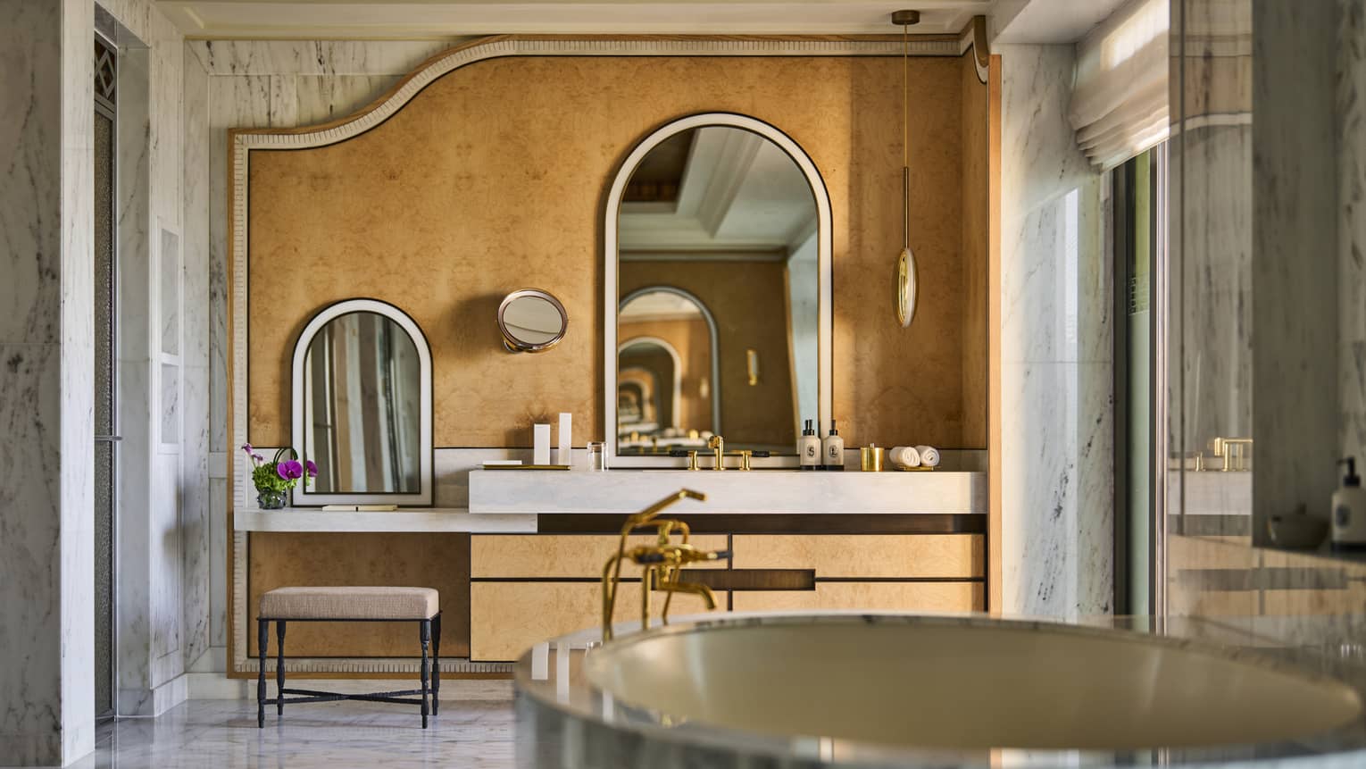 ,Large suite bathroom with free-standing oval marble bathtub, marble walls and a vanity area with two seats and arched mirrors