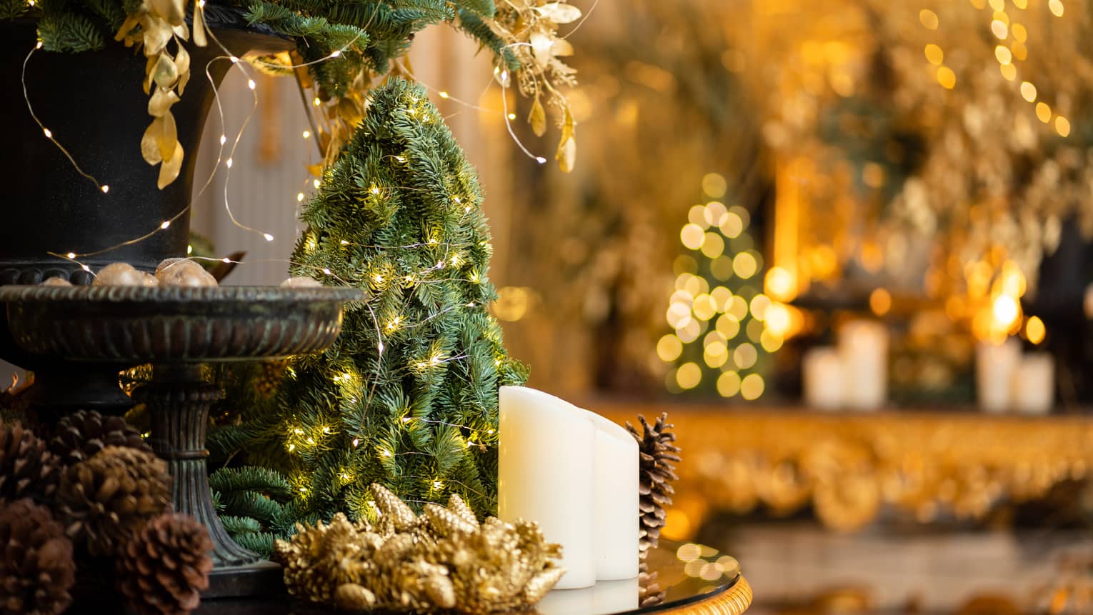 Arrangement of gold-lit mini Christmas trees, white candles and pinecones