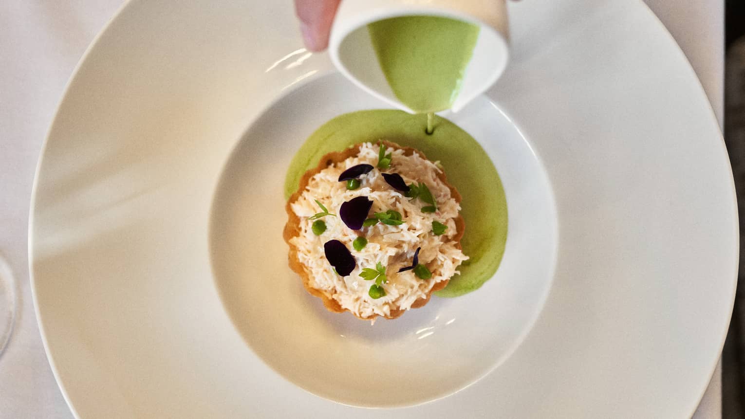 Crab tournedos on crust and garnished with shaved black truffle and herbs with green sauce being poured over