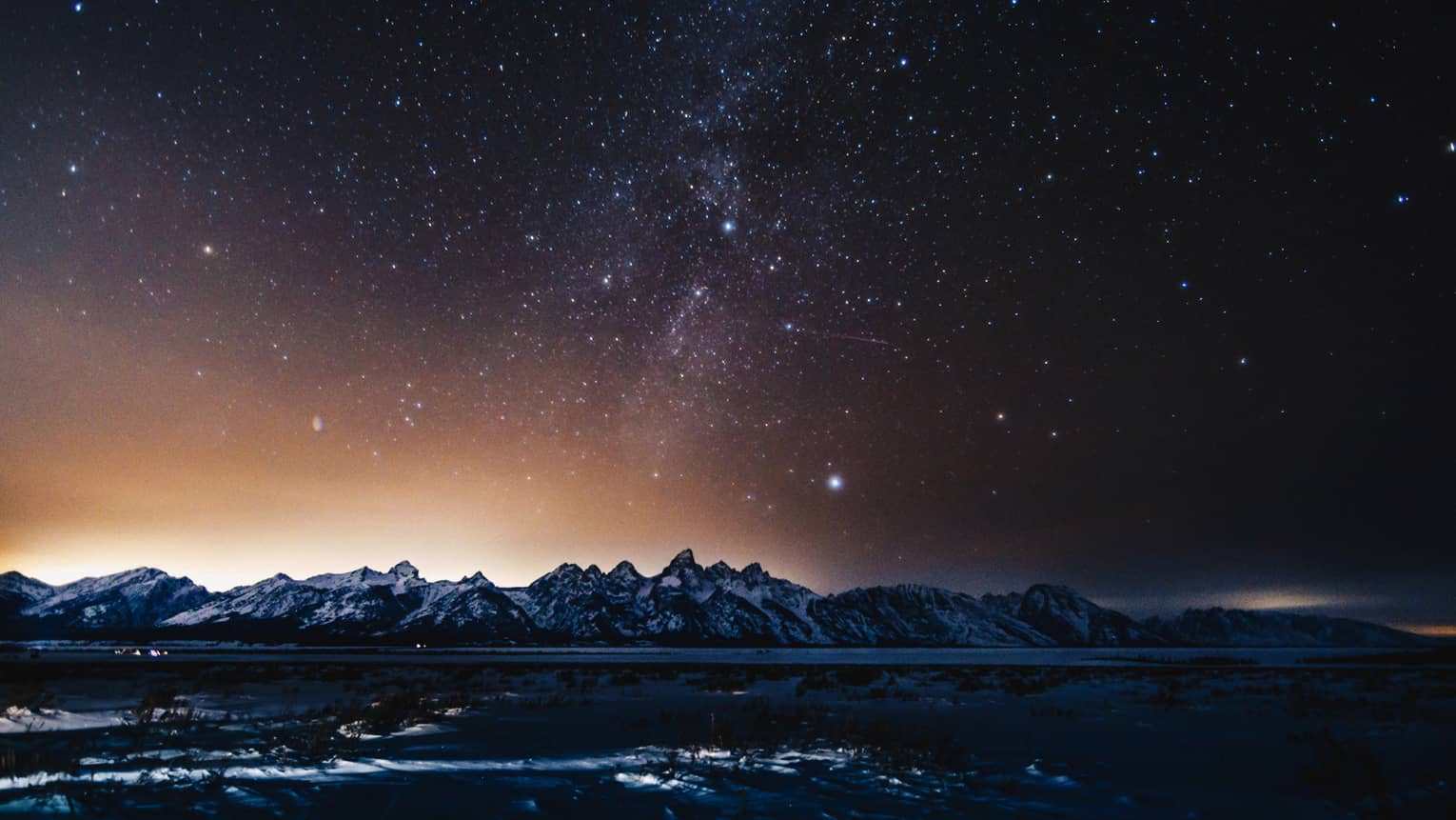 silhouette of mountains and solar flare across the starry night sky in winter