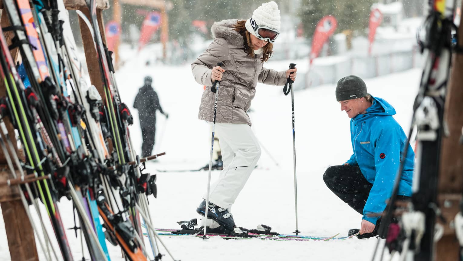 Ski concierge kneels down by woman trying on skis in front of rack