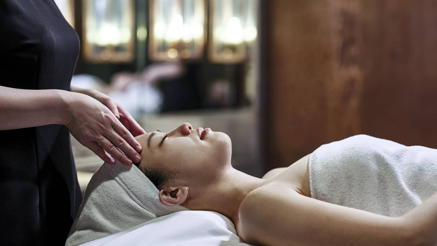 Woman getting a head massage during spa treatment, white towel over her and her head