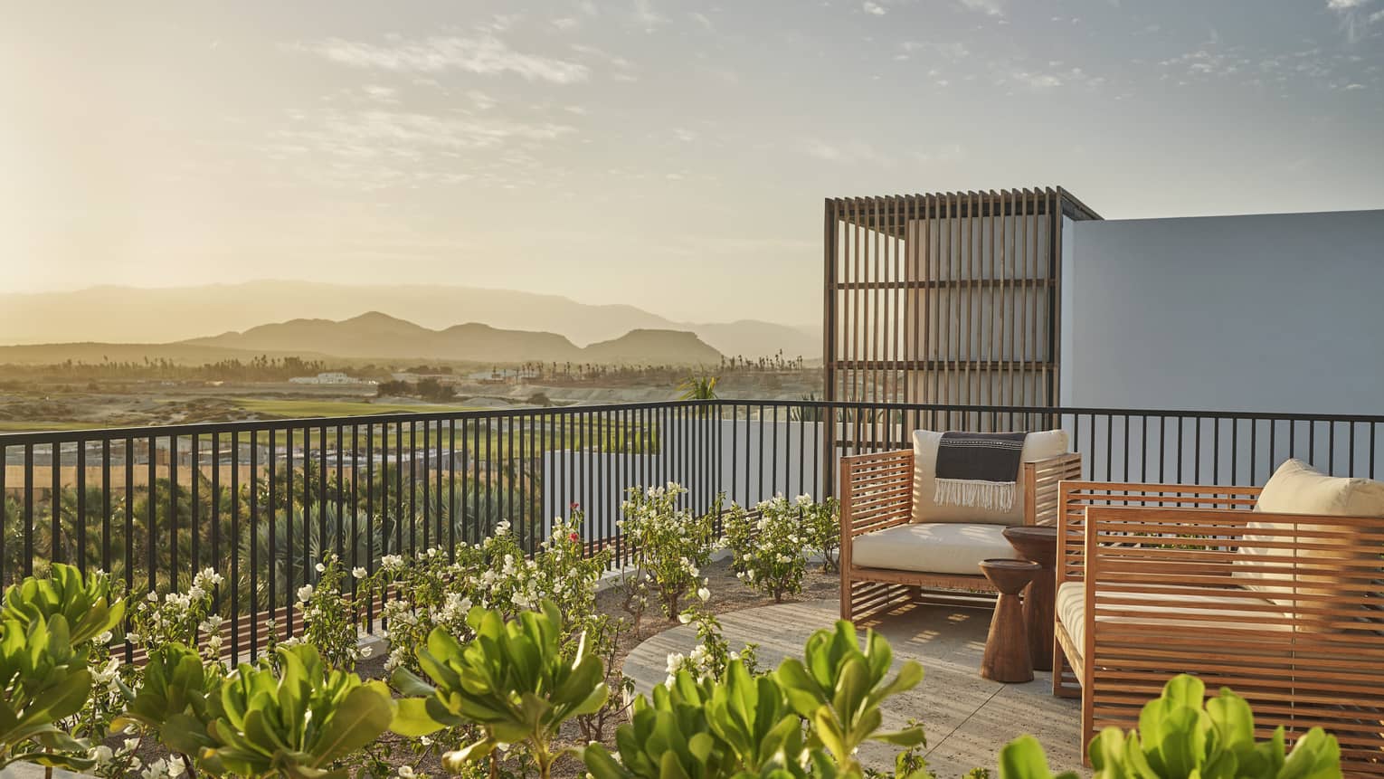 Rooftop terrace with two modern wooden arm chairs, Los Cabos view at dusk