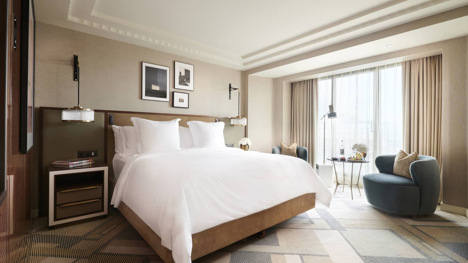 Deluxe room at the Four Seasons London Park Lane in Mayfair, featuring a spacious and well-appointed interior. The room includes a large king-sized bed with white linens and plush pillows, flanked by bedside tables and elegant wall-mounted lamps. A cozy seating area near the window includes a stylish blue armchair and a small circular table with chairs, ideal for relaxing or enjoying the view. The room's decor is enhanced by soft, neutral curtains, tasteful artwork on the walls, and a sophisticated, modern design.,Deluxe Room at Four Seasons London Park Lane in Mayfair, featuring a spacious and well-appointed interior. The room includes a large king-sized bed with white linens and plush pillows, flanked by bedside tables and elegant wall-mounted lamps. A cosy seating area near the window includes a stylish blue armchair and a small circular table with chairs, ideal for relaxing or enjoying the view. The room's decor is enhanced by soft, neutral curtains, tasteful artwork on the walls and a sophisticated, modern design.