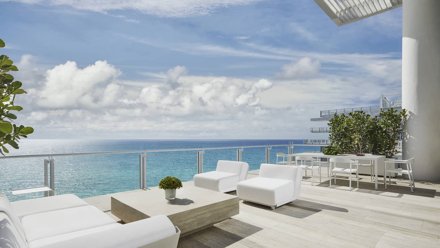Modern white patio sofas, table on large, sunny deck overlooking blue ocean at Four Seasons Hotel at the Surf Club, Surfside, providing luxury vacation rentals in Miami.