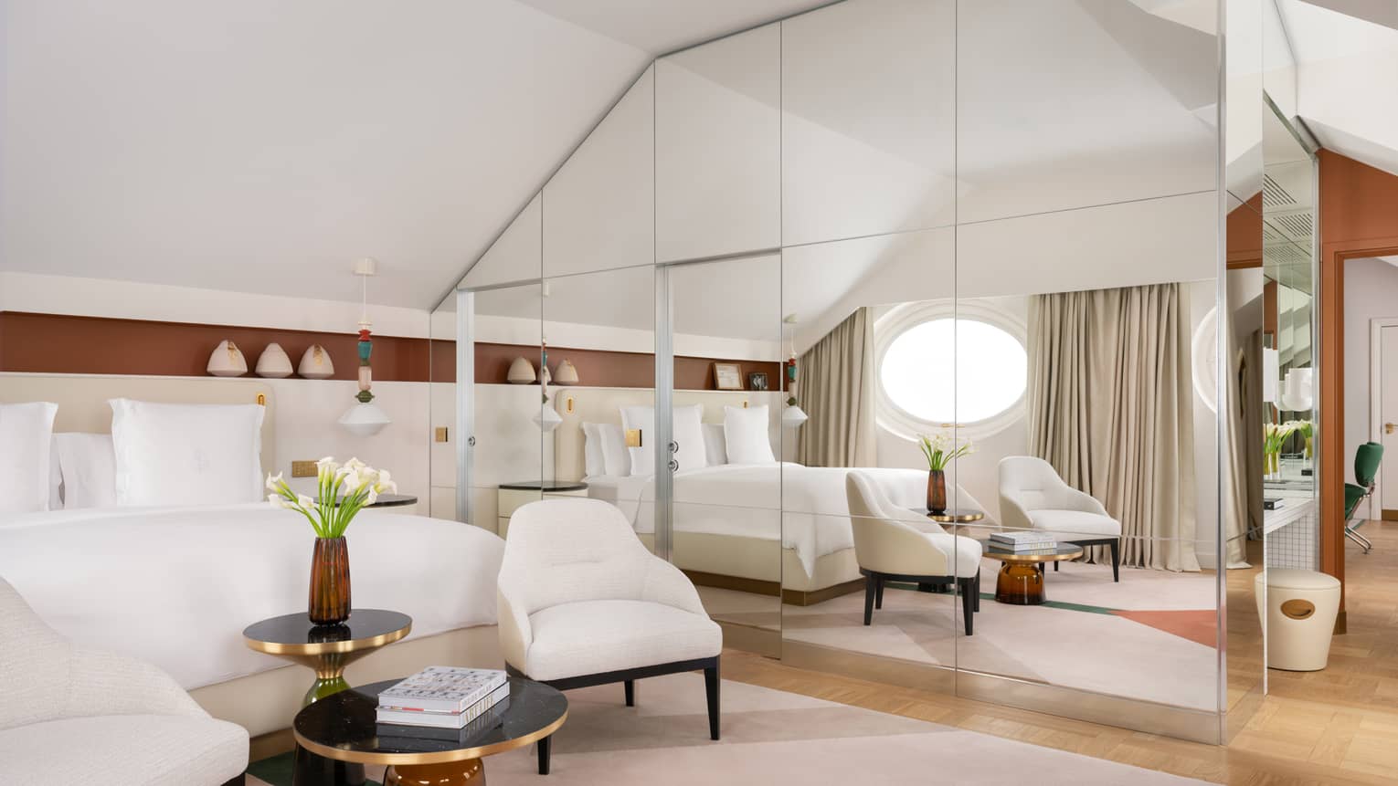 Contemporary hotel suite featuring a king bed, two ivory-coloured arm chairs and a glass wall