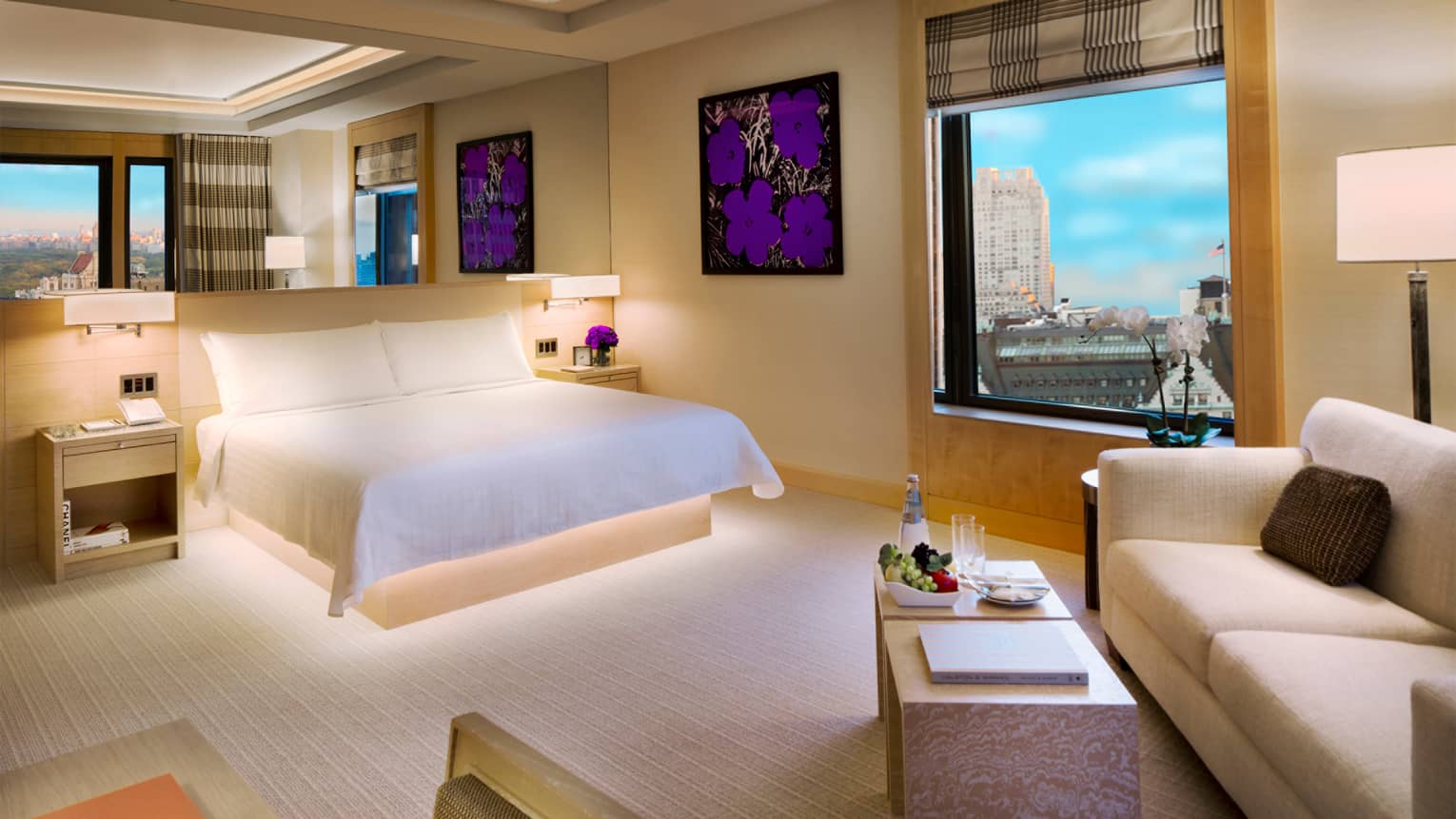 Modern Manhattan Junior Suite with framed purple flower print, white bed, sofa, window with park view