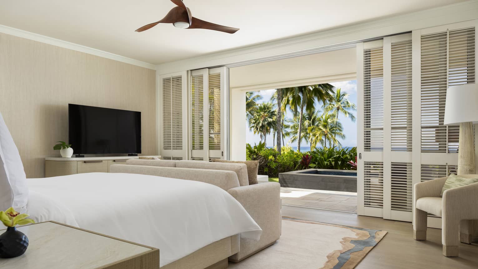 Luxury resort suite bedroom featuring a king bed facing shuttered sliding doors with walk-out ocean-view terrace