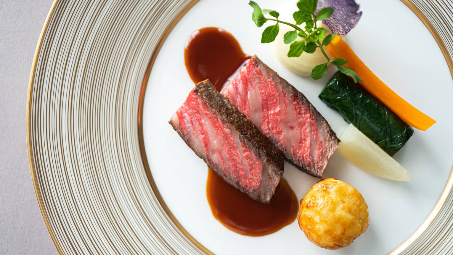 Aerial shot of grilled NY strip steak (rare) with demi-glace and vegetable garnishes