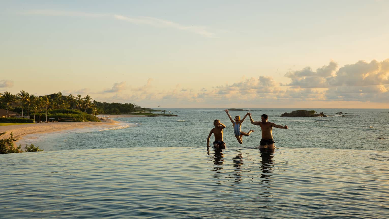 Three people including one child play in infinity pool overlooking the ocean and beach