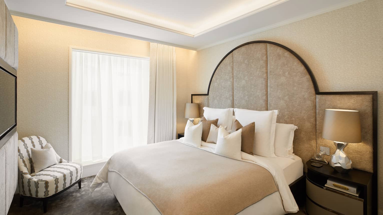 Secondary bedroom with king bed and large headboard, window and arm chair, in the Penthouse Suite at Four Seasons Hotel London at Ten Trinity Square
