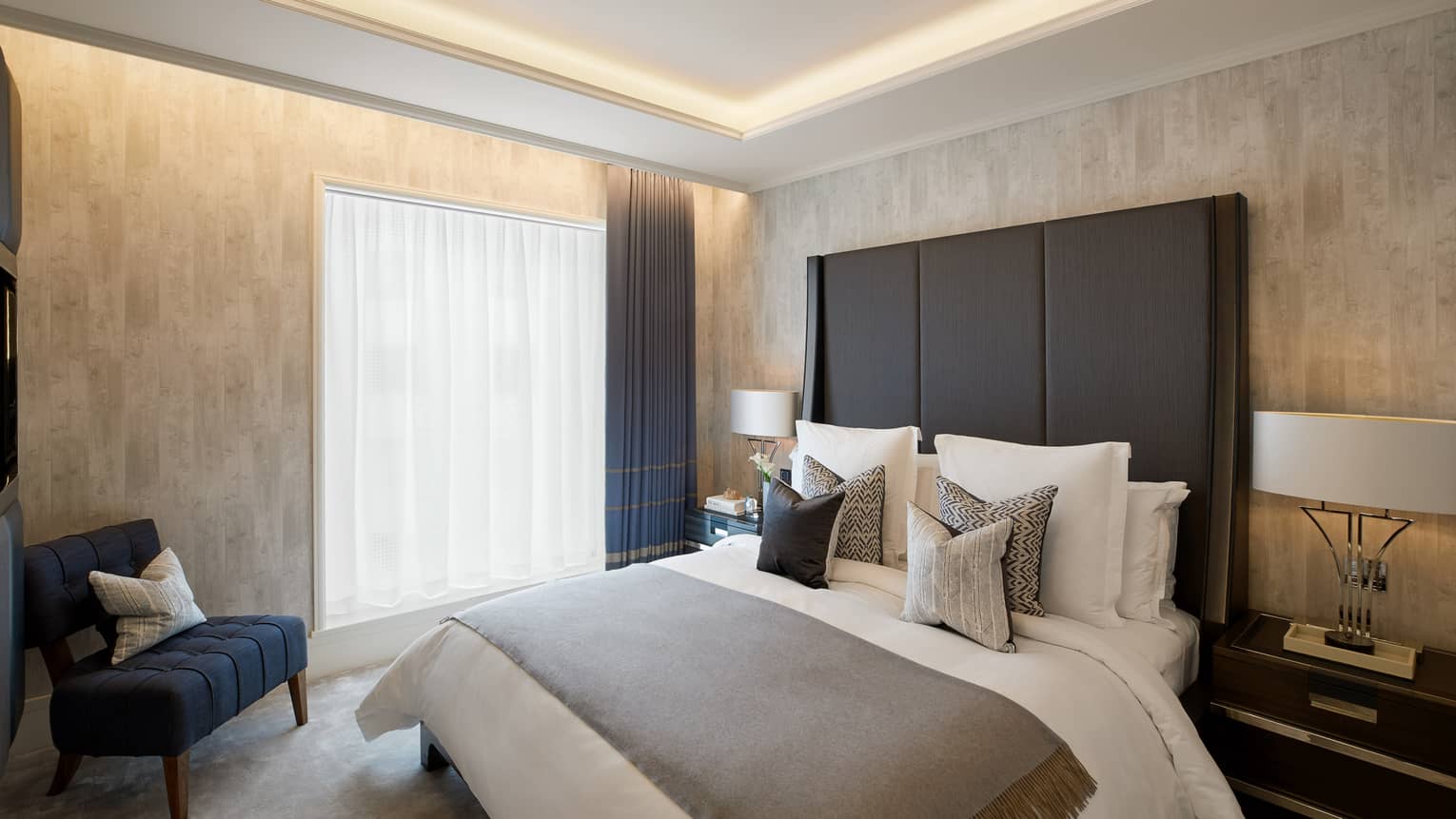 Secondary bedroom with king bed and large headboard, window and arm chair, in the Penthouse Suite at Four Seasons Hotel London at Ten Trinity Square