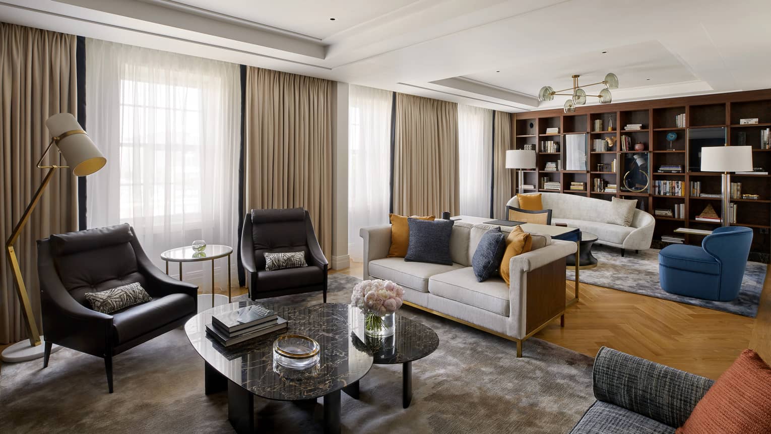 Living area with two black chairs and coffee table, grey loveseat in front of living area with white sofa, blue chair