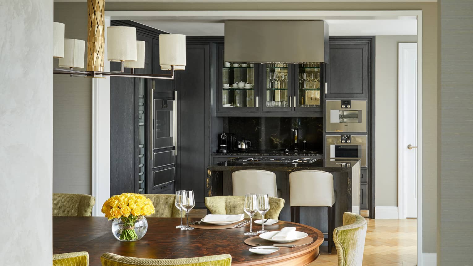 A dining and kitchen area with large wood table, counter with stools and cabinets with glass doors.