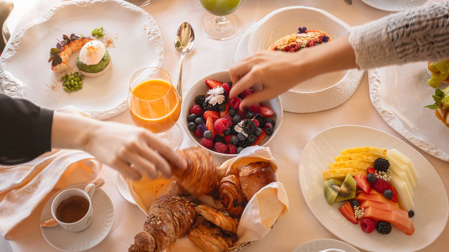 Two hands picking up brunch foods from spread of dishes