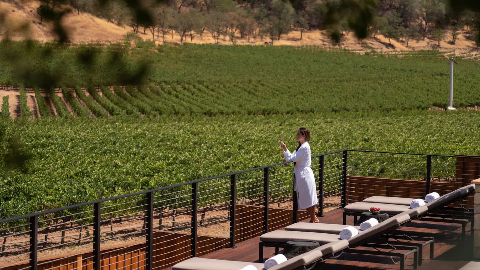 Person wearing a robe and holding a wine glass while admiring the views from the Spa sun deck.