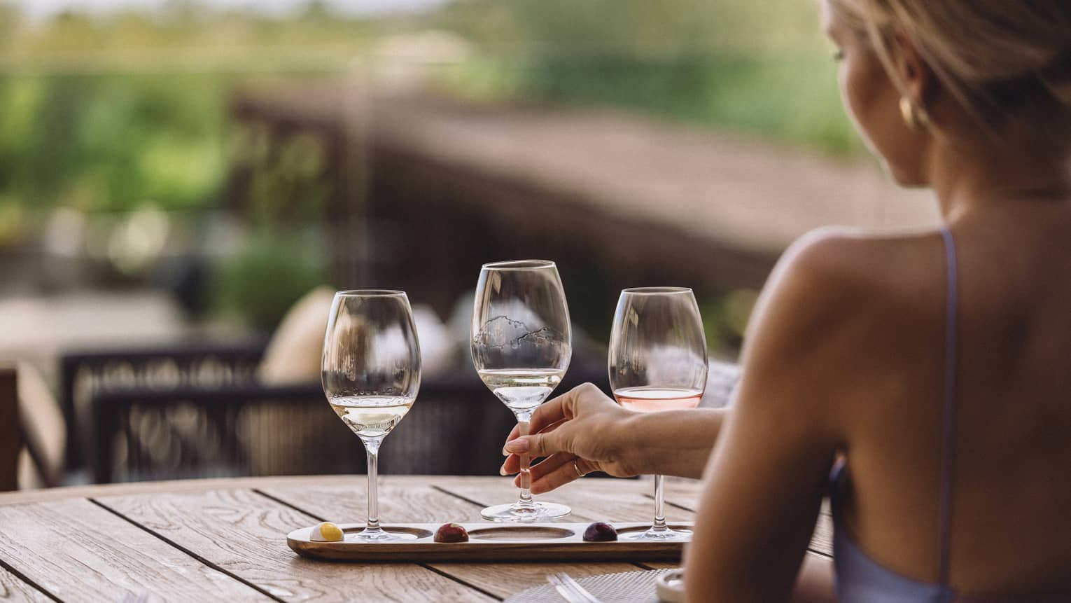 Person sitting at an outdoor table reaching for one of three wine glasses.