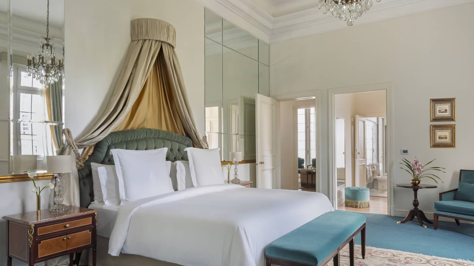 Elegant suite bedroom with king bed, draped canopy, and turquoise velvet bench and chair