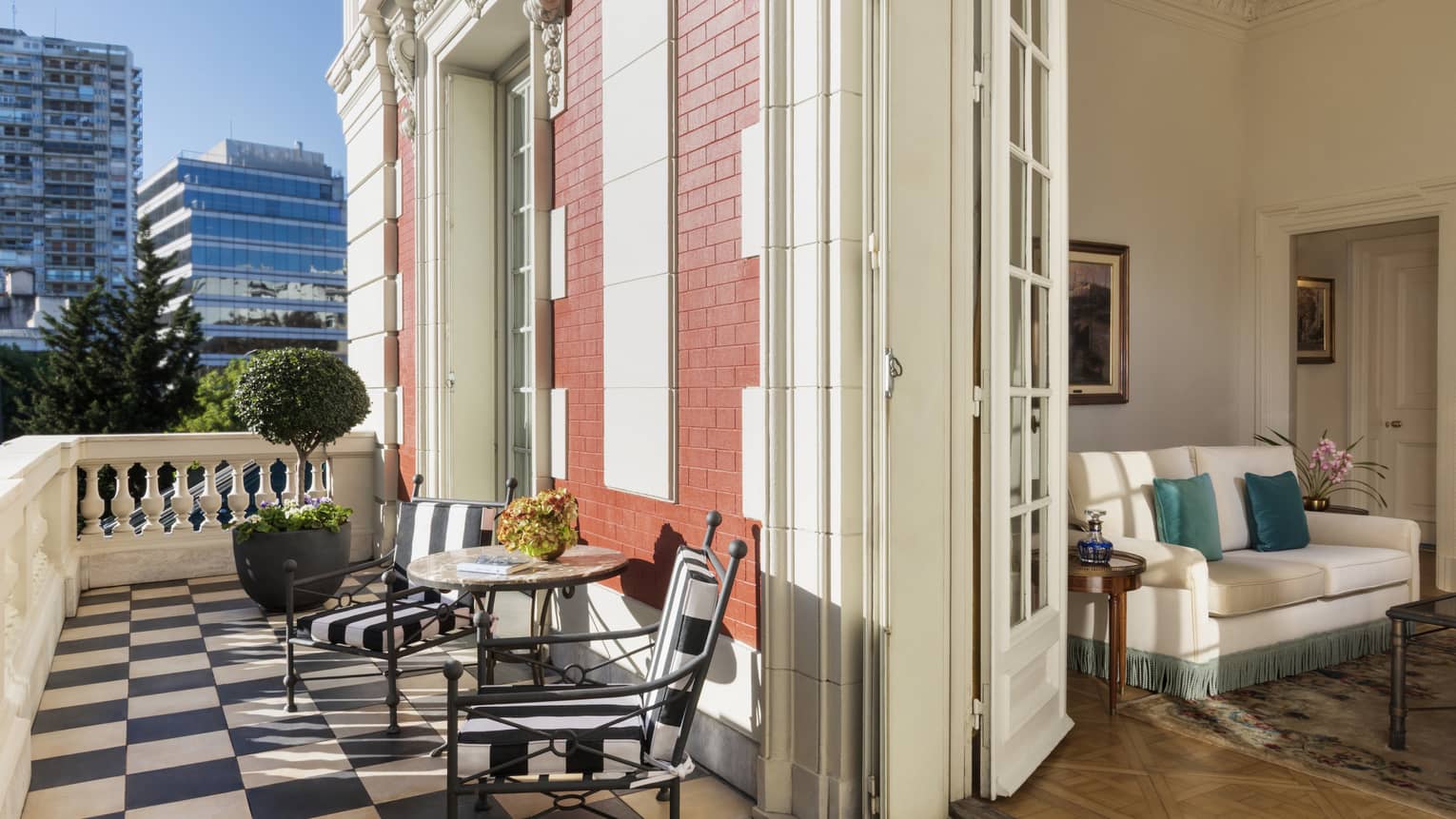 Hotel suite living room opens up to a private balcony with black-and-white checkered tile flooring and views of the city