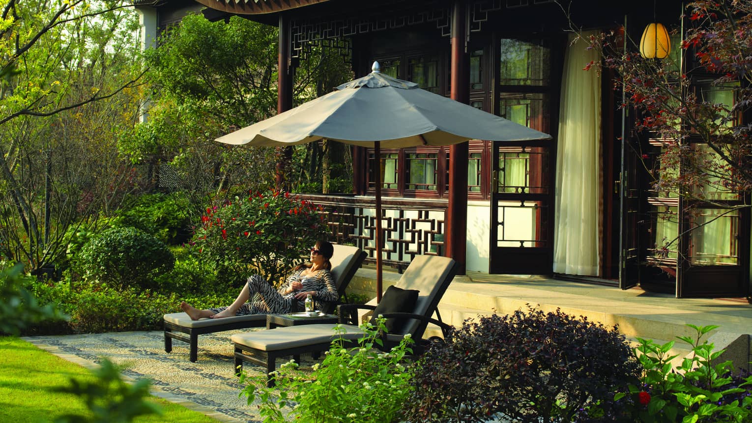 Royal West Lake Suite woman in zebra-striped outfit under umbrella on patio lounge chair