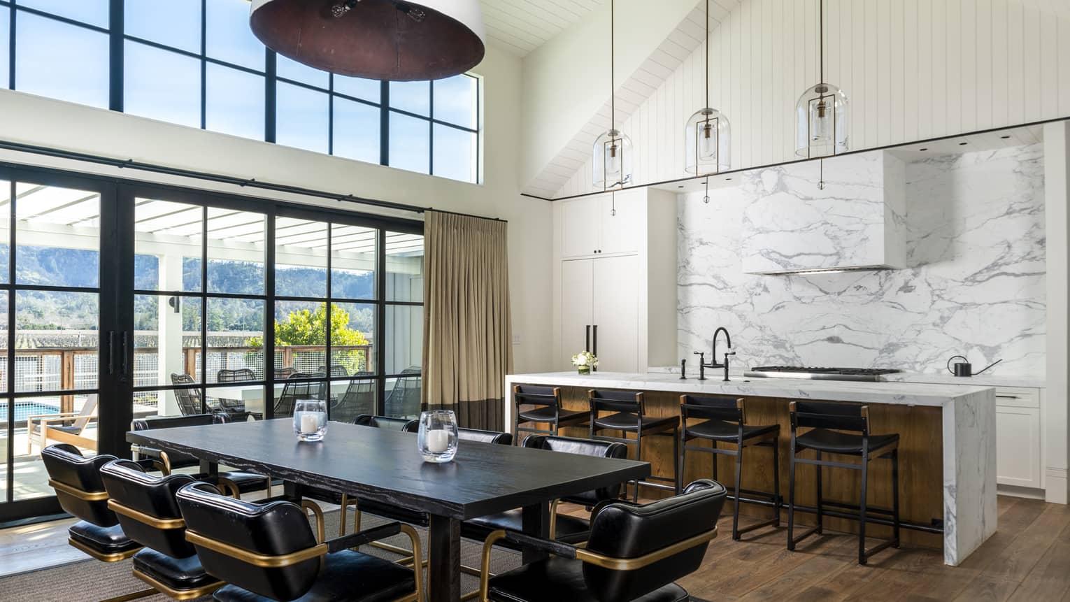 Luxury resort kitchen and dining area with a marble island, dining table, high ceilings and large glass doors opening to an outdoor patio with mountain views