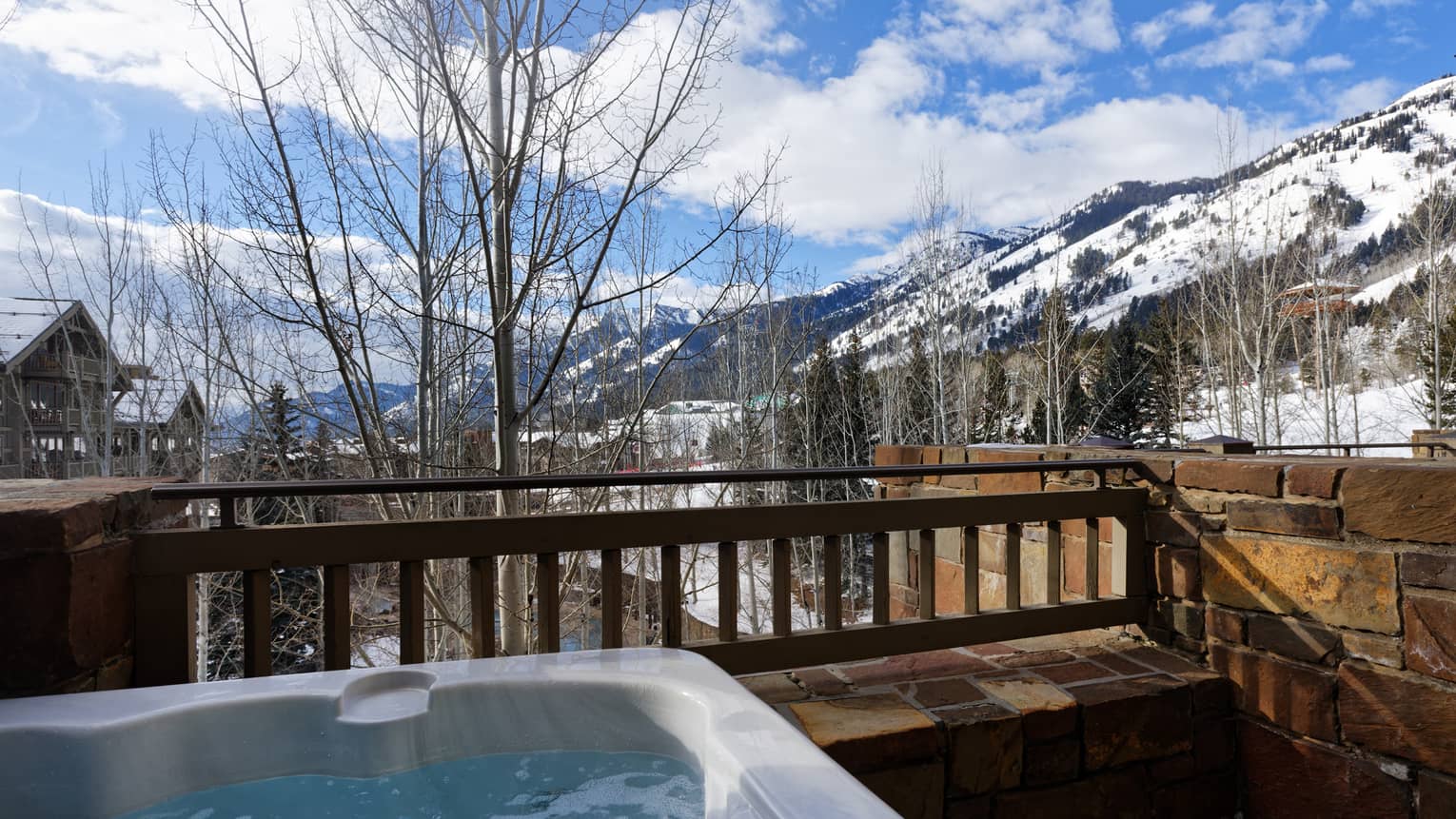 Outdoor hot tub on a stone patio with a scenic snow-covered mountain view at a luxury resort