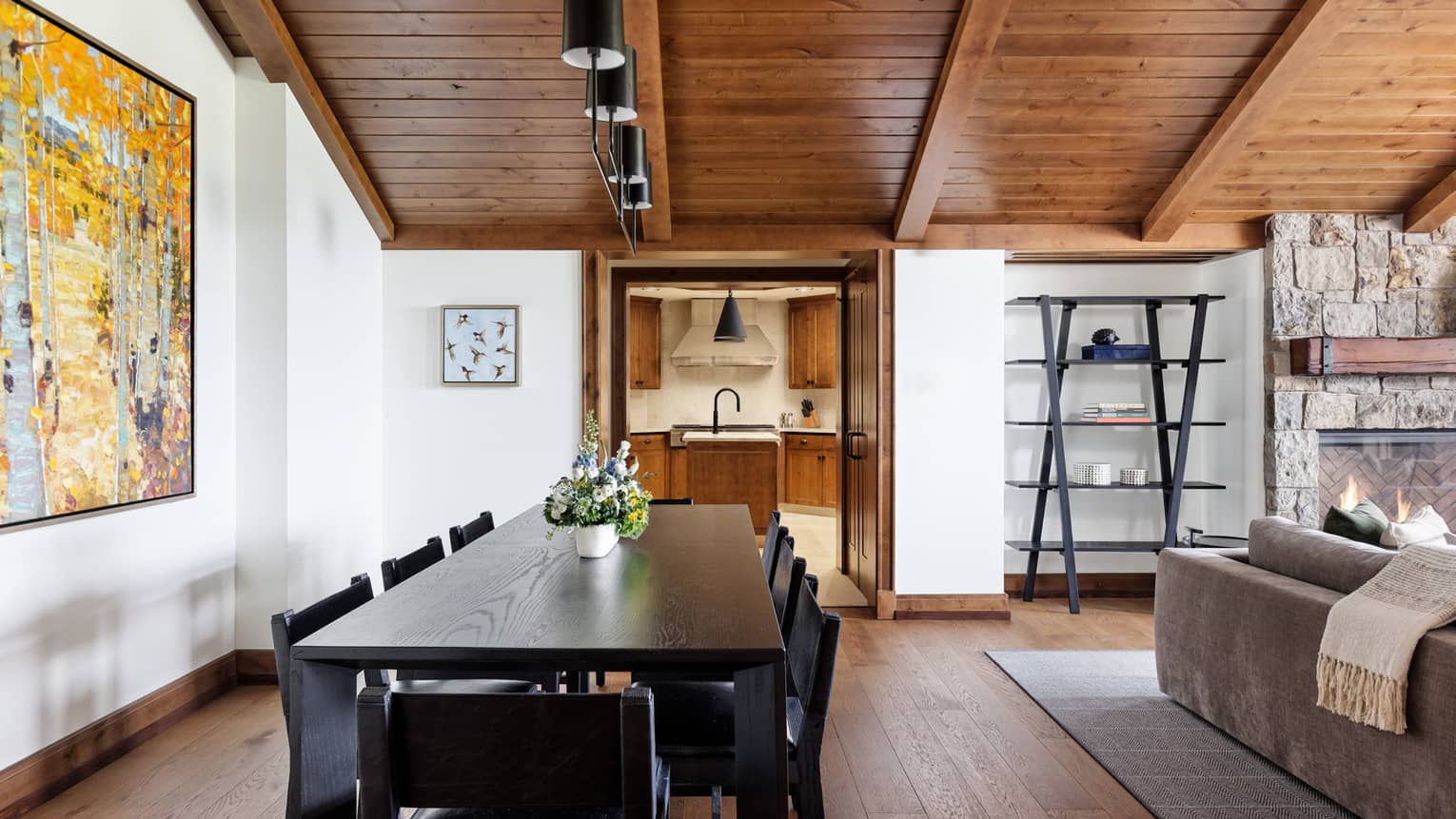 Dining area with wooden floors and ceiling, dark wooden table with eight chairs, artwork and stone hearth