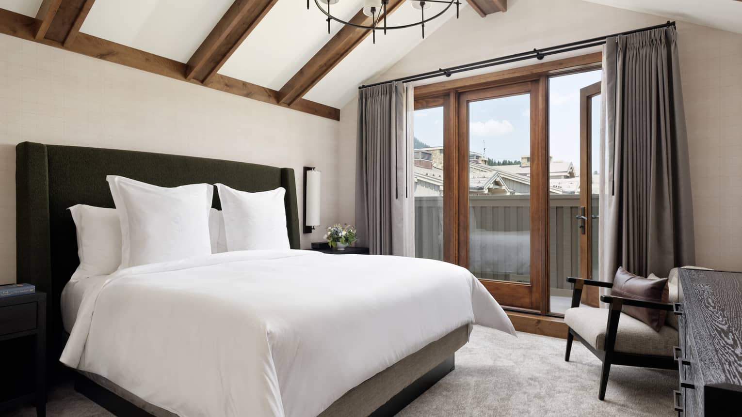 Luxury resort bedroom with king bed, armchair, walk-out balcony and vaulted wood-beam ceiling
