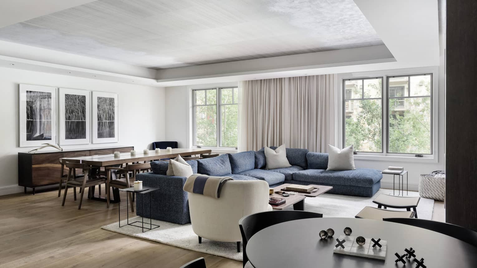 Living room of hotel residence, featuring a large dark blue sectional sofa and two different dining spaces