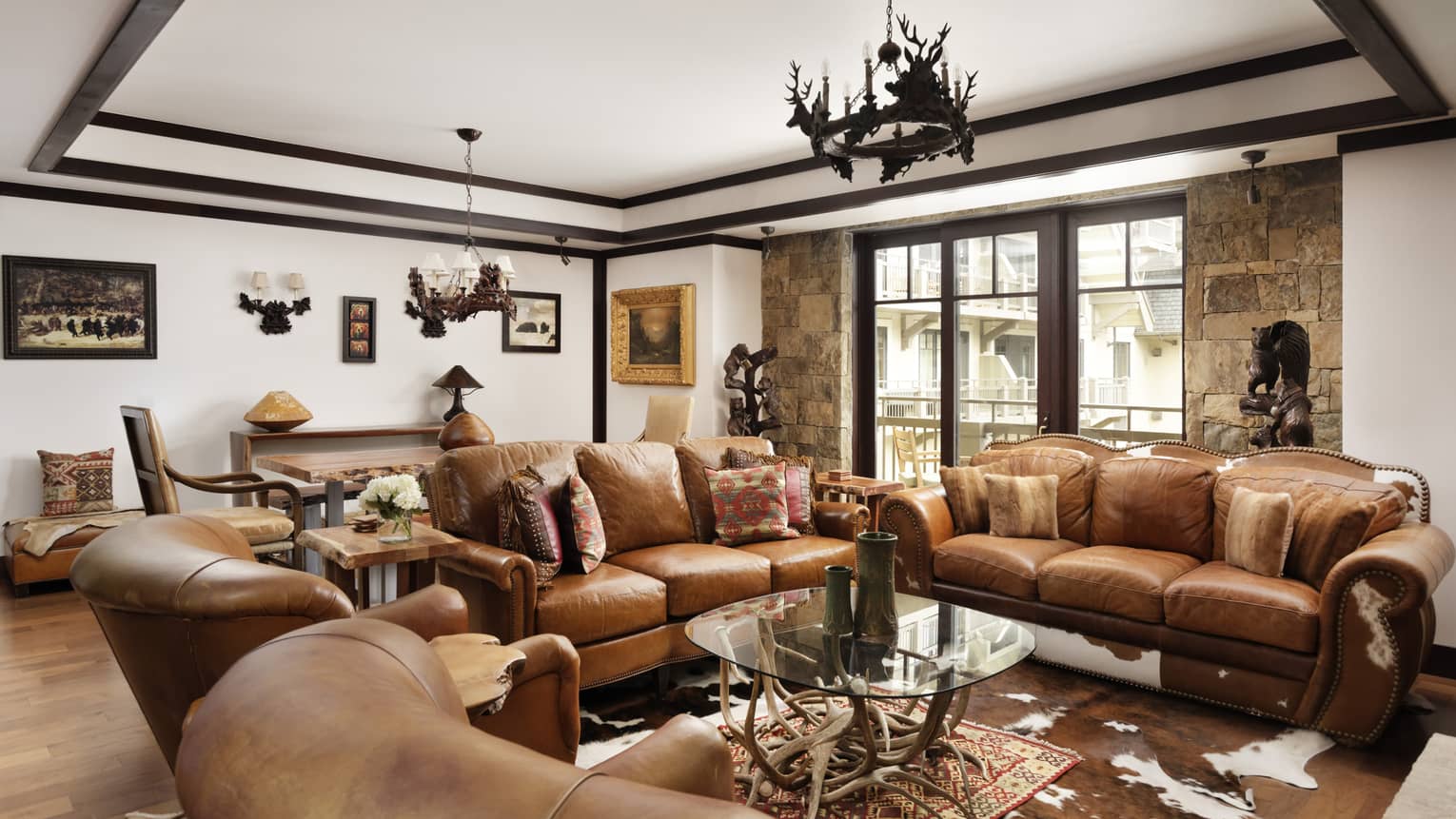 Mountain-chic living room with two brown leather sofas, two matching arm chairs, antler chandelier