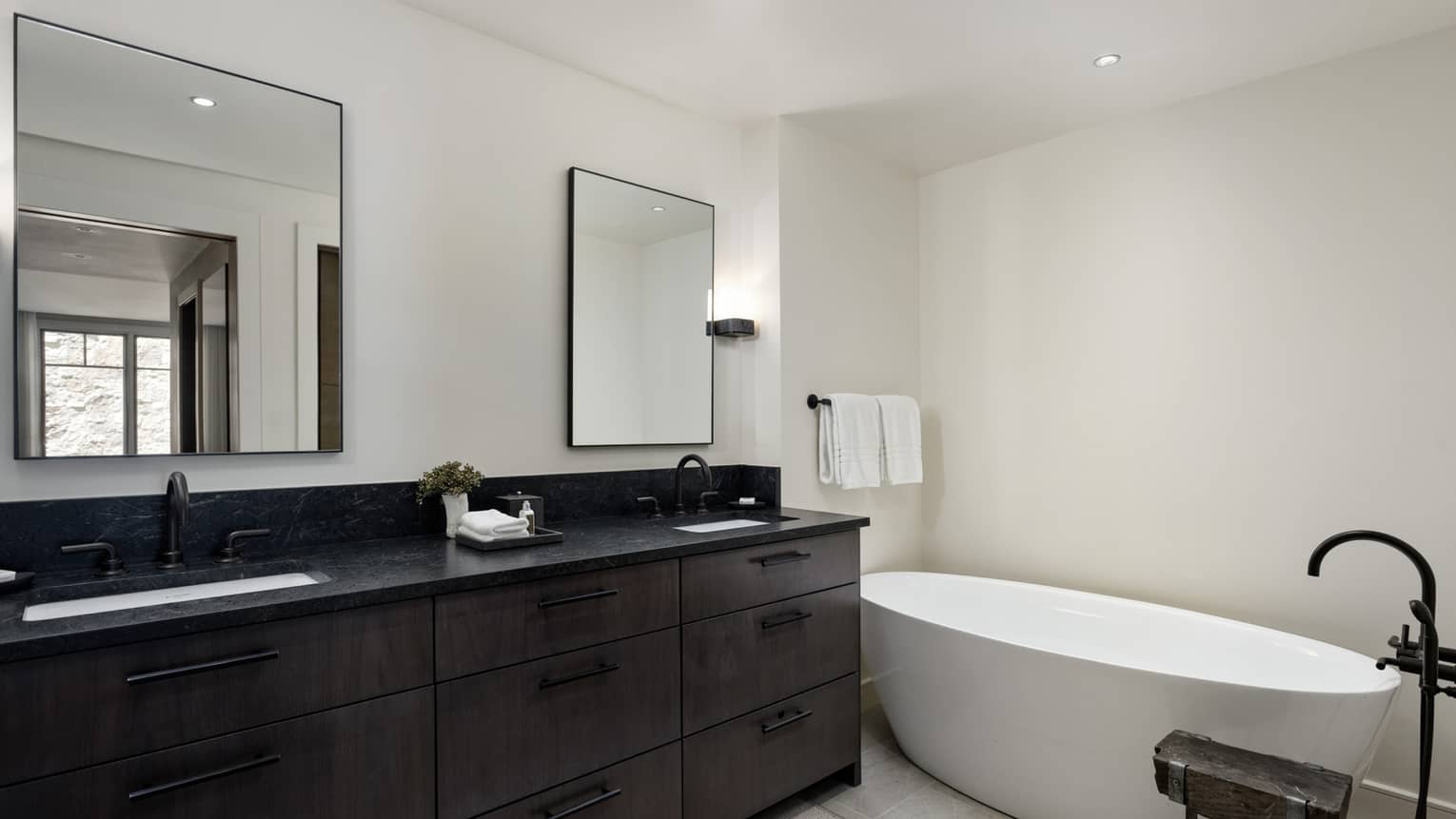 Modern bathroom with deep soaking tub and double vanity with black counter