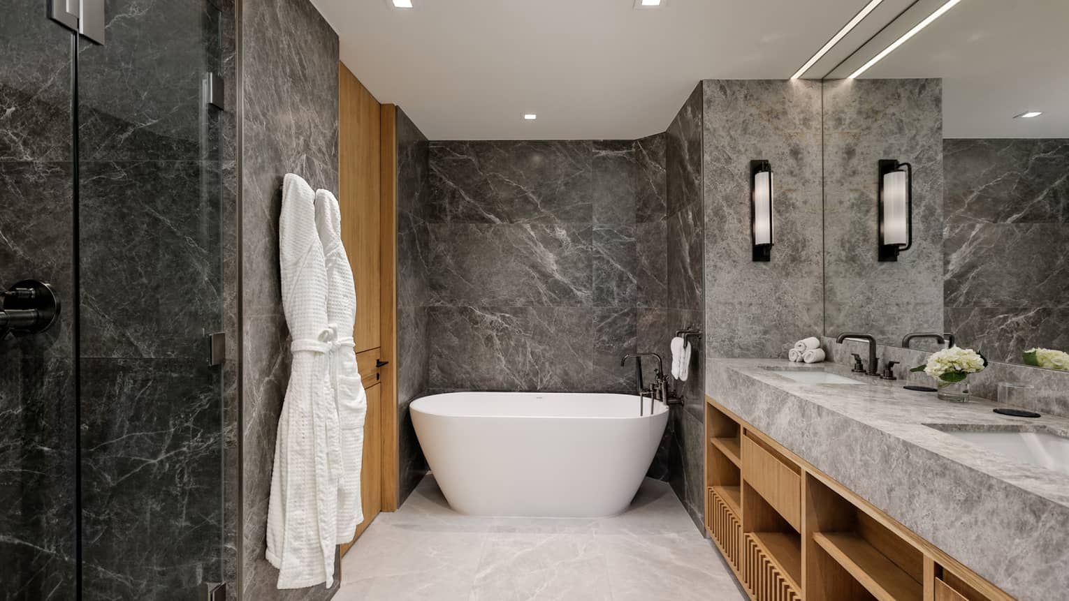 Sleek marble bathroom with standalone deep soaking tub and two hanging bathrobes