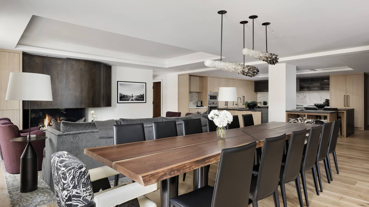 Large dining table with 12 chairs in a contemporary private residence, set next to living room with wooden floors and fireplace