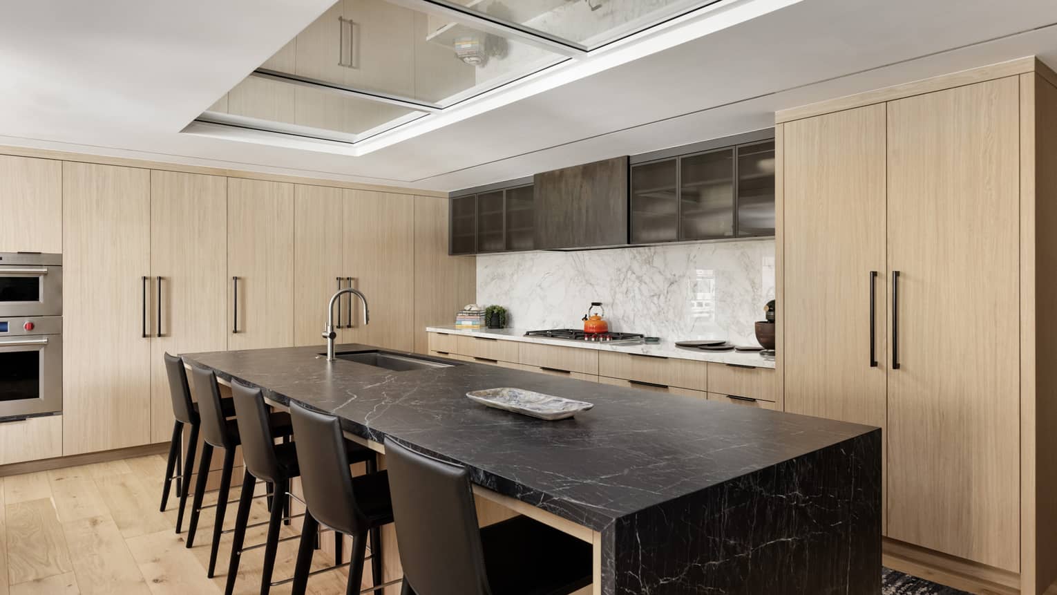 Modern kitchen with light wood cabinets and dark marble island with six counter-height chairs