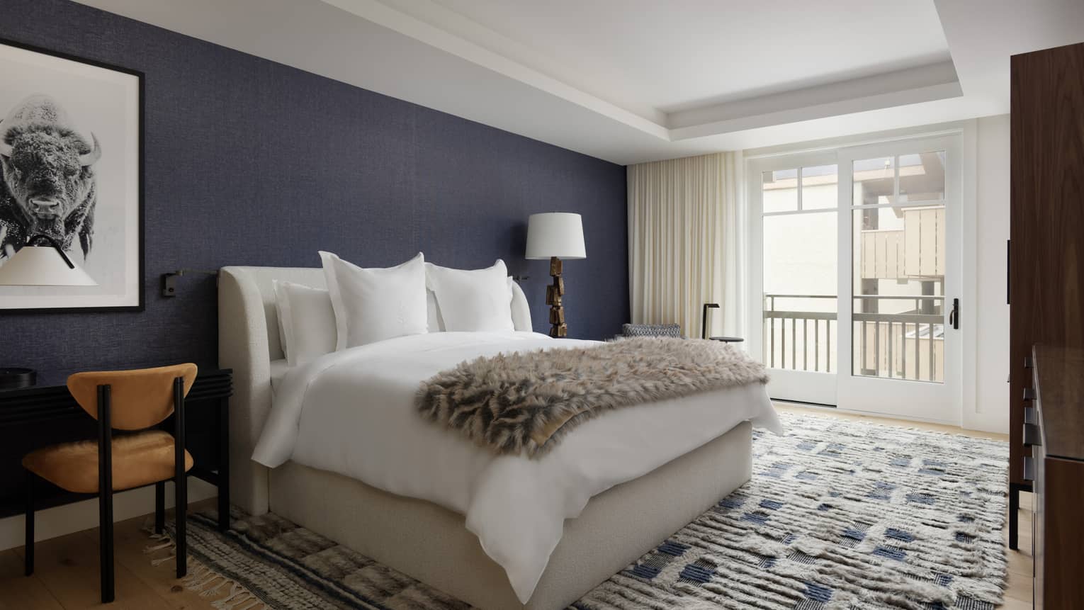 Stylish bedroom with king bed, blue and white accent rug, dark blue accent wall, sliding door to balcony