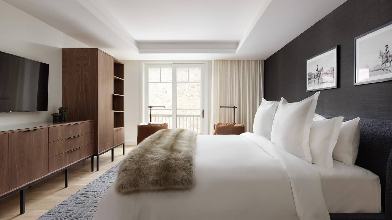 Stylish bedroom with king bed, faux fur blanket, dark blue accent wall, wooden dresser and sliding door to balcony