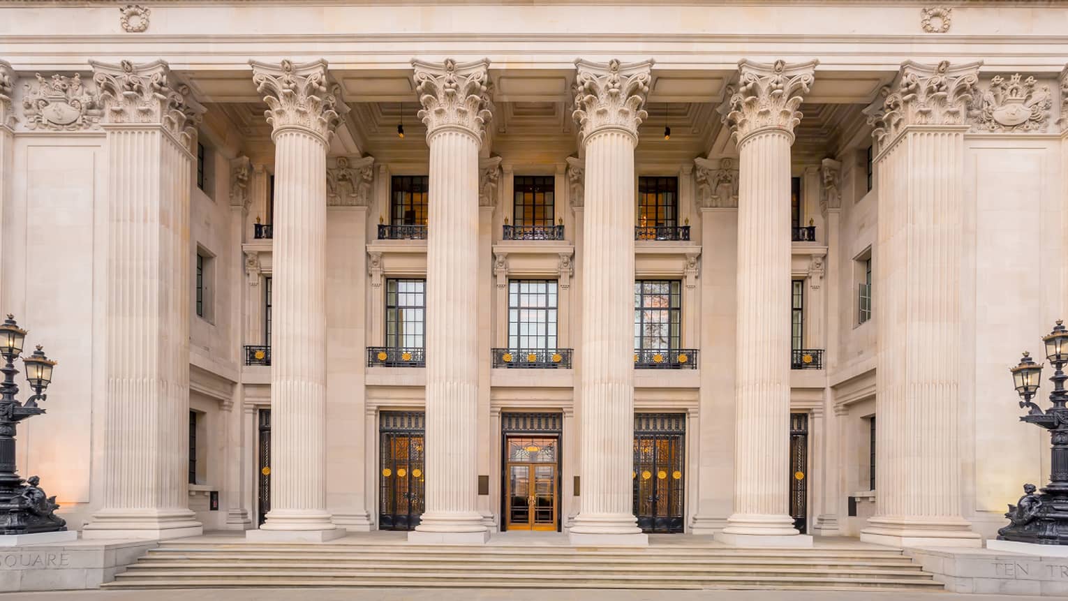 Large, three-storey white pillars in front of glass windows with decorative gold trim