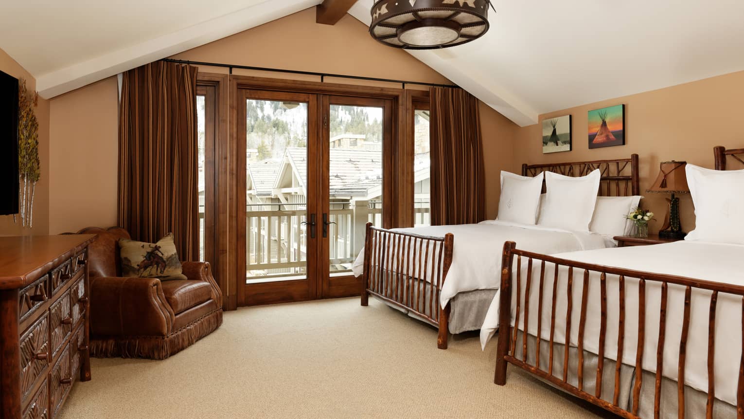 Bedroom with two rustic wooden beds, vaulted ceiling, leather armchair and doors opening to a balcony