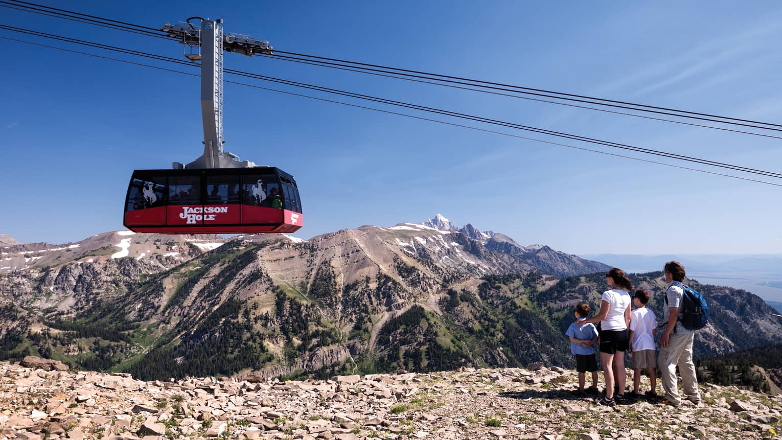 A family of four watches from a cliff as a ski lift passes by