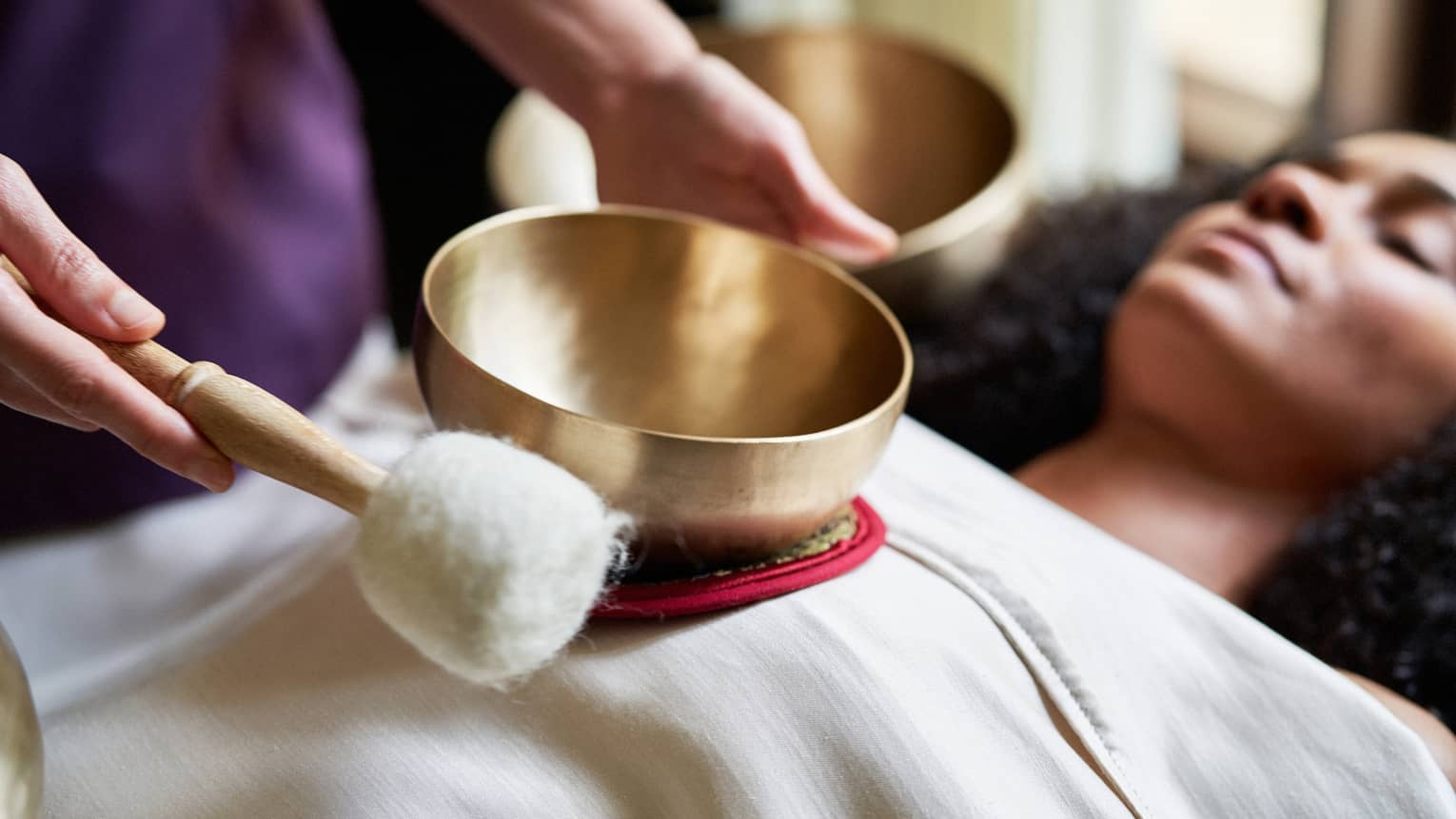 A woman with a sheet on her and a spa team member holding a golden bowl over her.