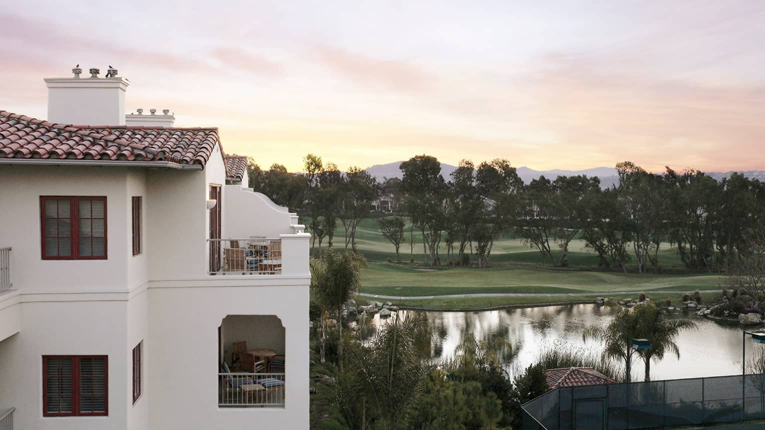 Pink sky over manicured lawn and trees, pond and white building