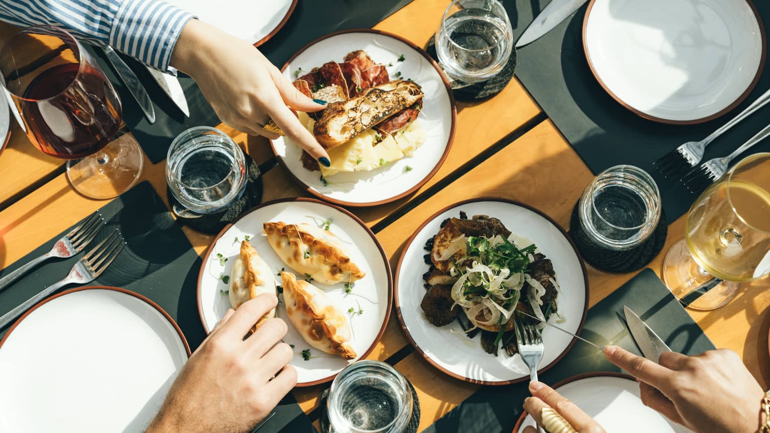 Three pairs of hands reaching for food in the centre of a table