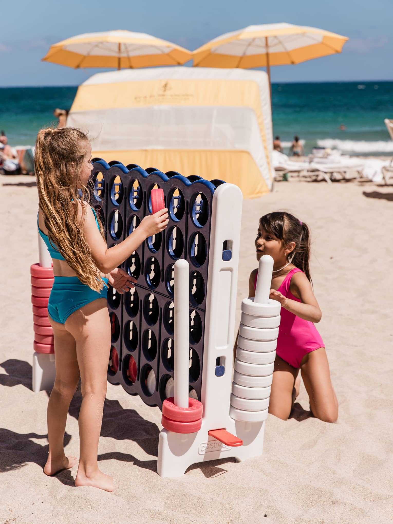 Two young kids play a giant Connect 4 game on the beach