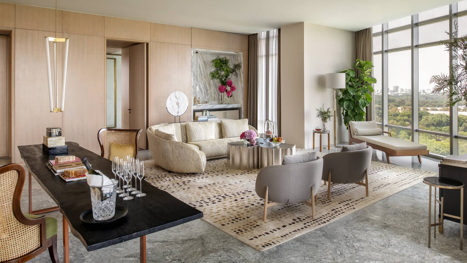 Guest room living area with cream sectional sofa, grey armchairs and chaise lounge, floor-to-ceiling windows, long rectangular black dining table