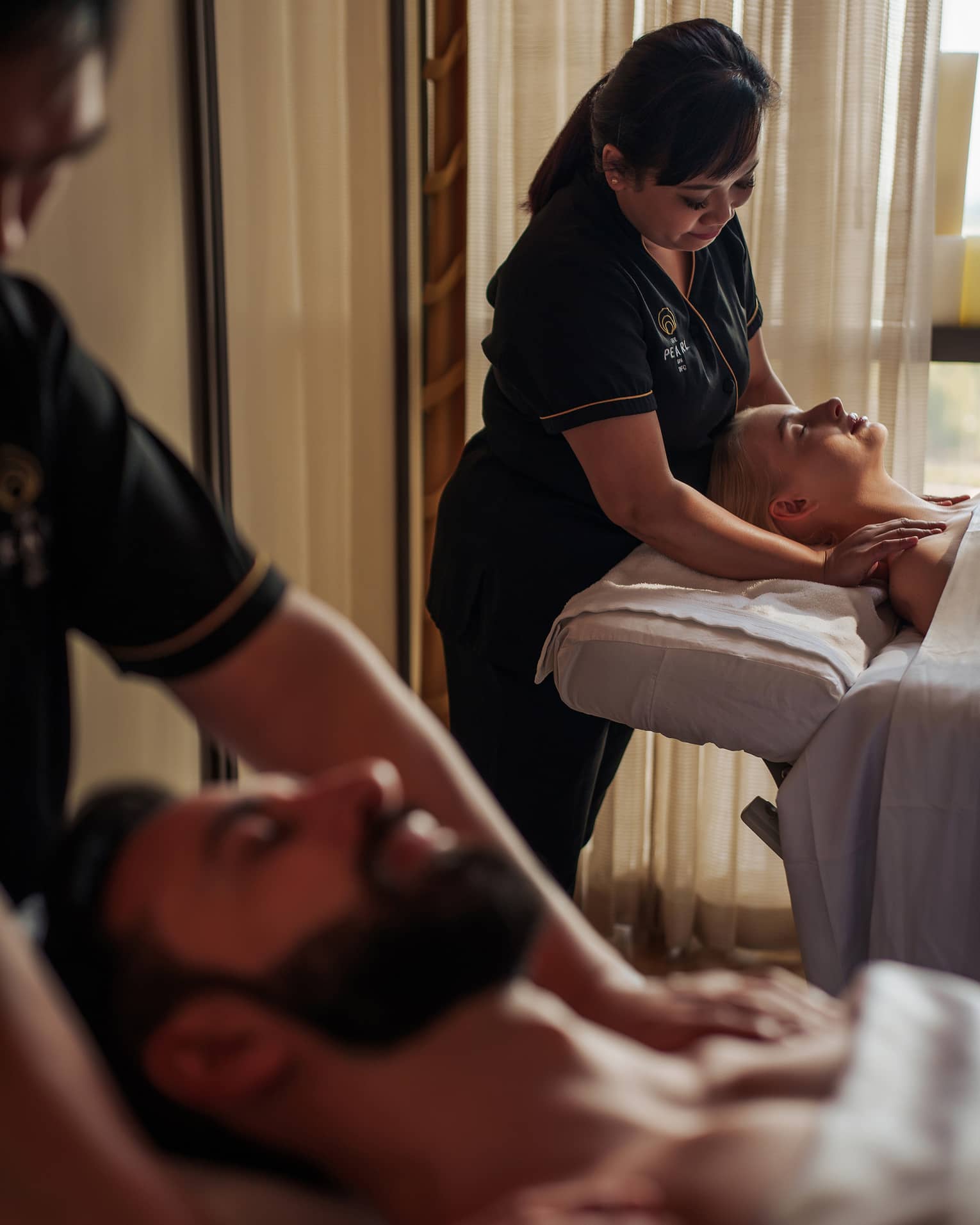 A two people receive a couple's massage in a serene spa treatment room.
